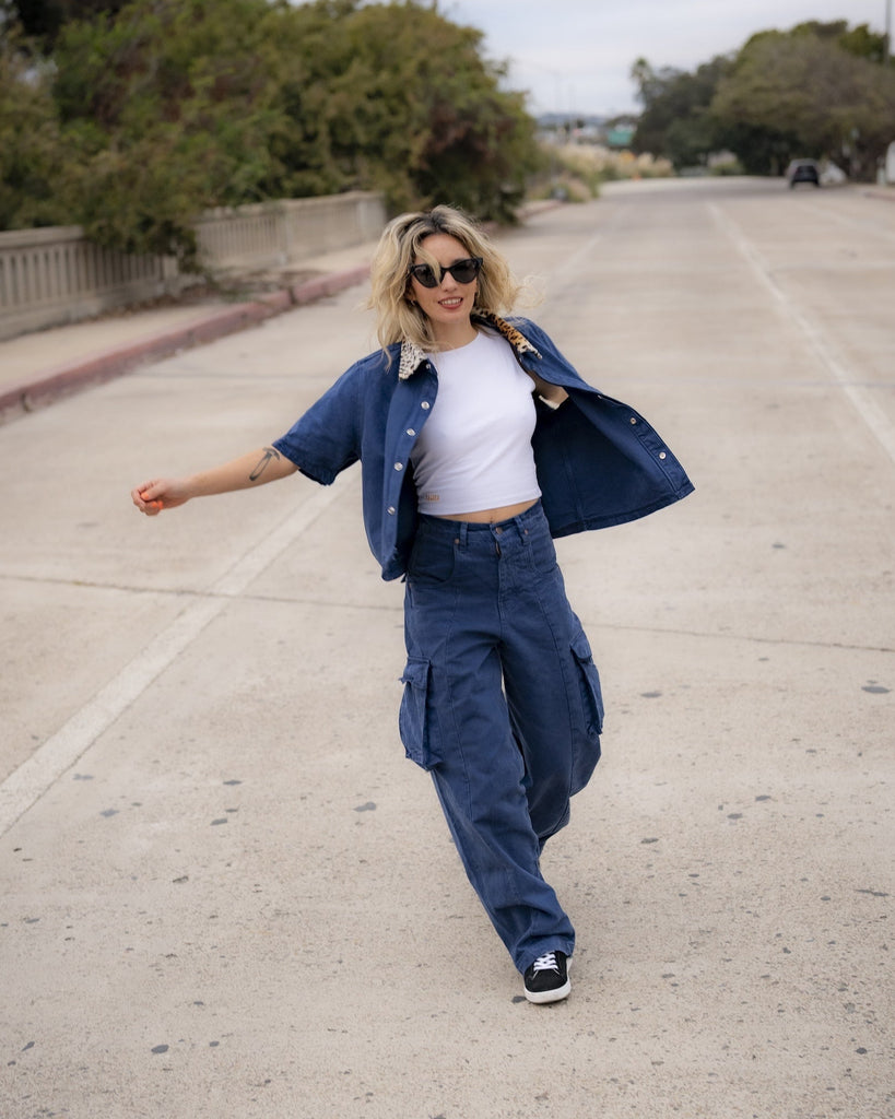 Woman in blue jacket and pants walking on a road with trees and power lines in the background